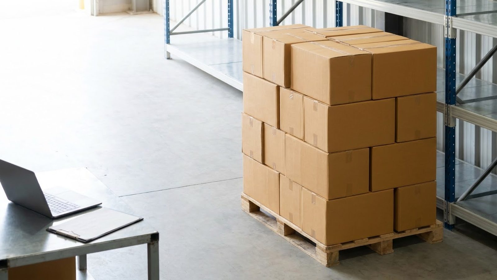 Industrial marketing agency for manufacturers: pallet of boxed product beside warehouse shelving, with a laptop on a nearby table